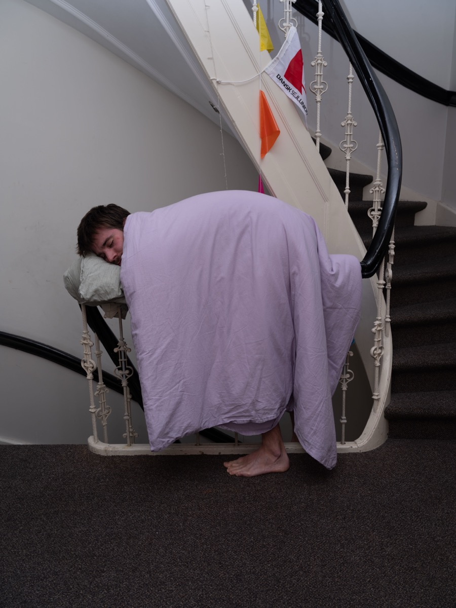 Luka Smišek asleep on a staircase landing, wrapped in a lilac duvet